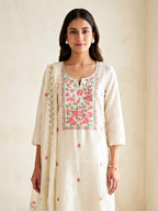 Cream floral cross-stitch cotton linen suit set with embroidered dupatta, featuring kurta, pants, and elegant floral embroidery.