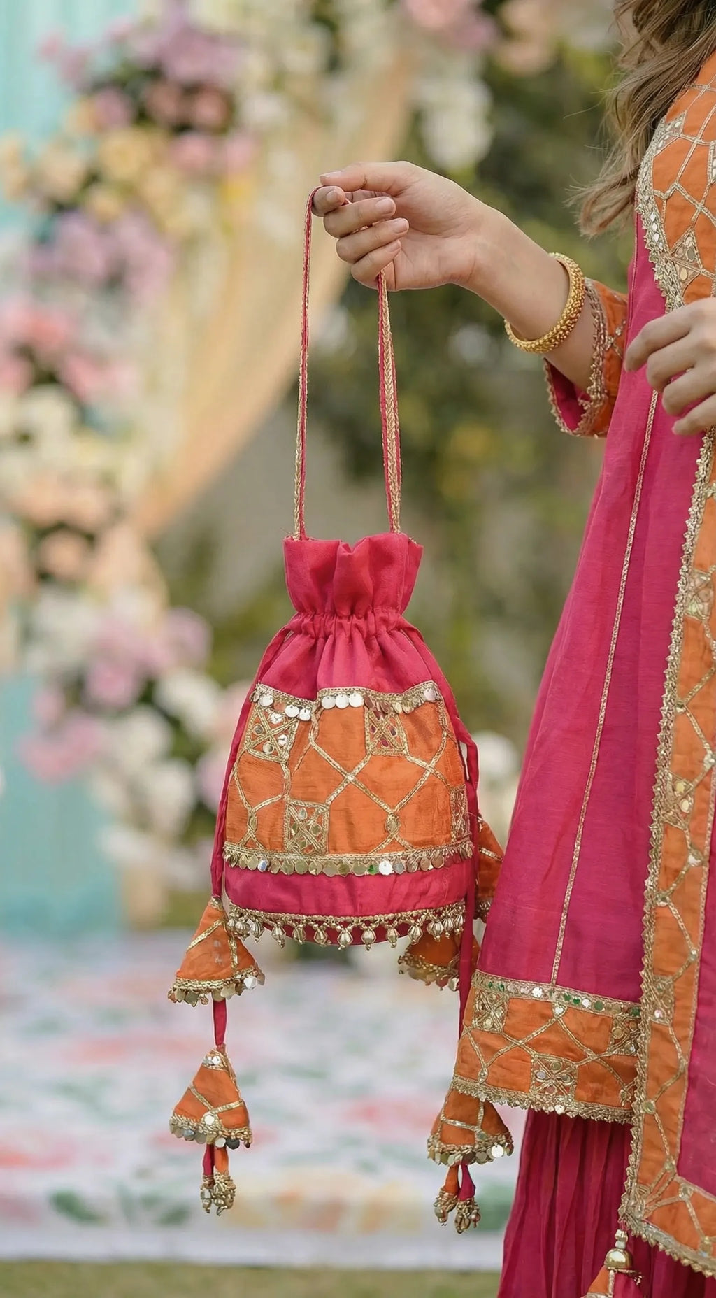 Hot pink and orange gota patti potli bag with sequin work, styled with an Anarkali sharara set from Karchobi women's clothing collection