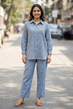 Woman wearing a light blue checkered linen cotton shirt and pant coord set on a street.