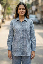 Woman wearing a blue checkered shirt pant coord set standing on a street.