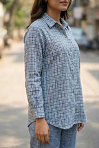 woman wearing a blue checkered shirt and pant coord set outdoors on a street.
