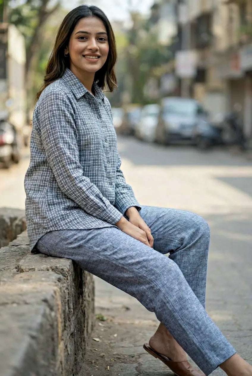 Woman sitting on a stone ledge outdoors wearing a checkered shirt and blue pants coord set for everyday wear.
