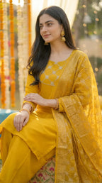 Woman in mustard yellow gota lace kurta and Afghani salwar set from Karchobi, sitting outdoors