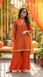 Woman modeling orange floral sequin embroidered kurta sharara set with lace trim from Karchobi, set in a festive outdoor decor.