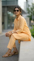 Woman wearing peach co-ord long shirt and pant set from Karchobi, seated outdoors