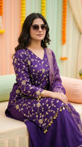 Woman wearing Karchobi purple floral sequin embroidered kurta sharara with dupatta, sitting elegantly.