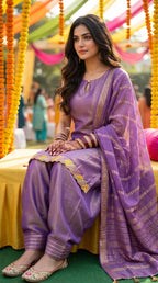 Woman wearing a purple sleeveless kurta and farshi salwar set with scalloped lace border, sitting at an outdoor event, showcasing Karchobi women's ethnic occasion wear.
