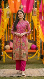 Woman wearing Karchobi rani pink floral zari embroidery achkan kurta pant set at a festive outdoor setting with vibrant drapes and marigold decor.