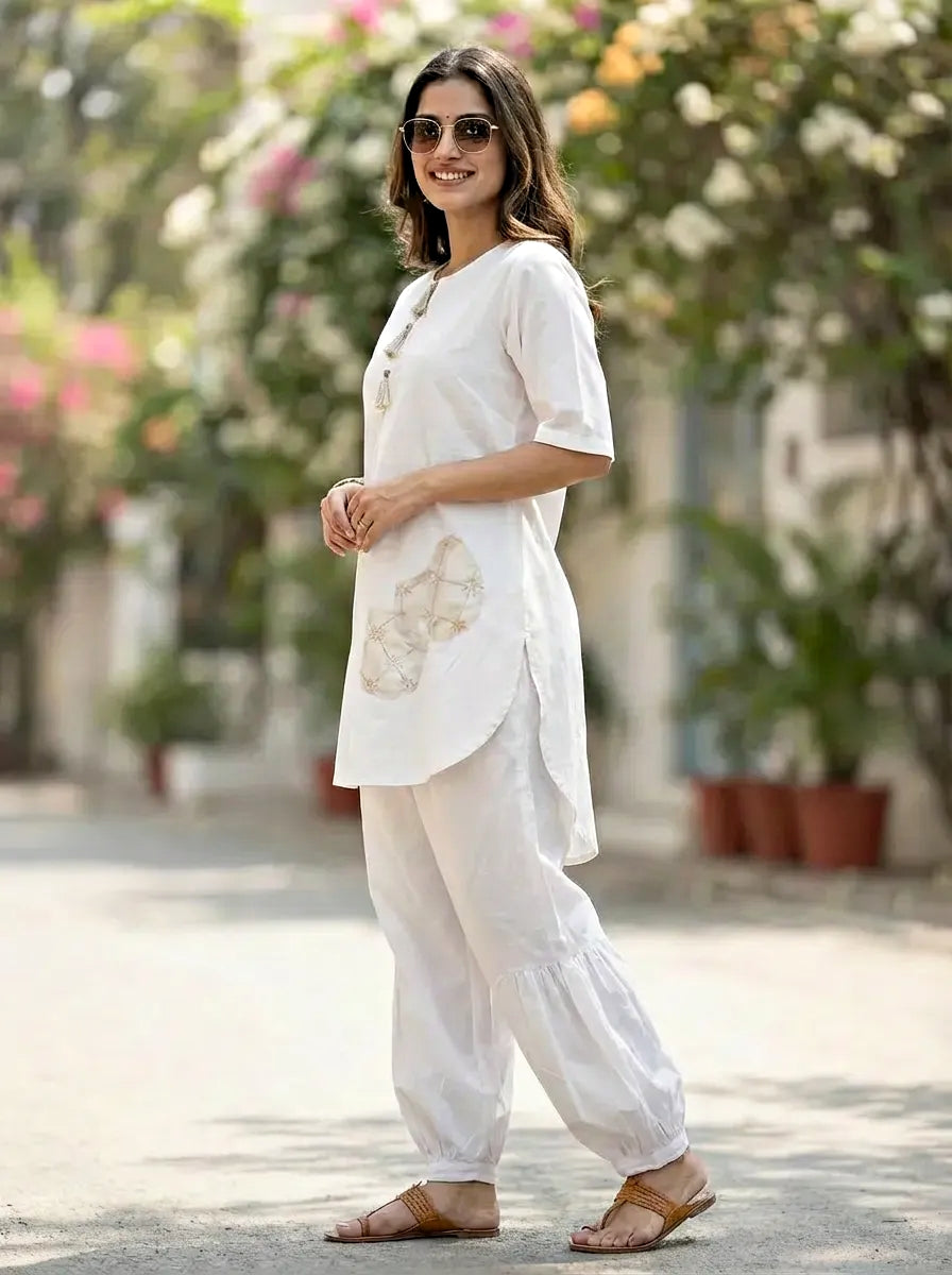 Woman in a White kurta Afghani salwar coord set standing outdoors with greenery in the background