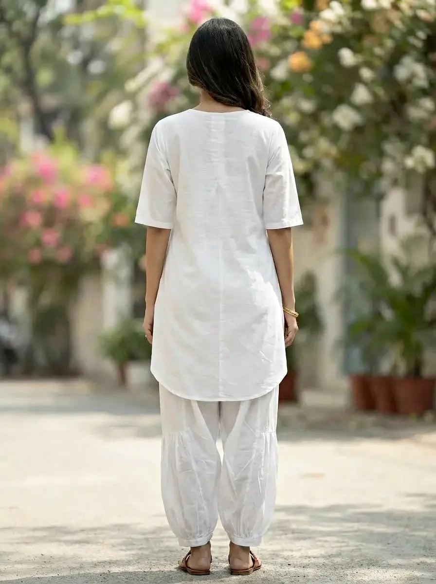 Woman wearing a white outfit walking outdoors with blurred flowers and plants in the background
